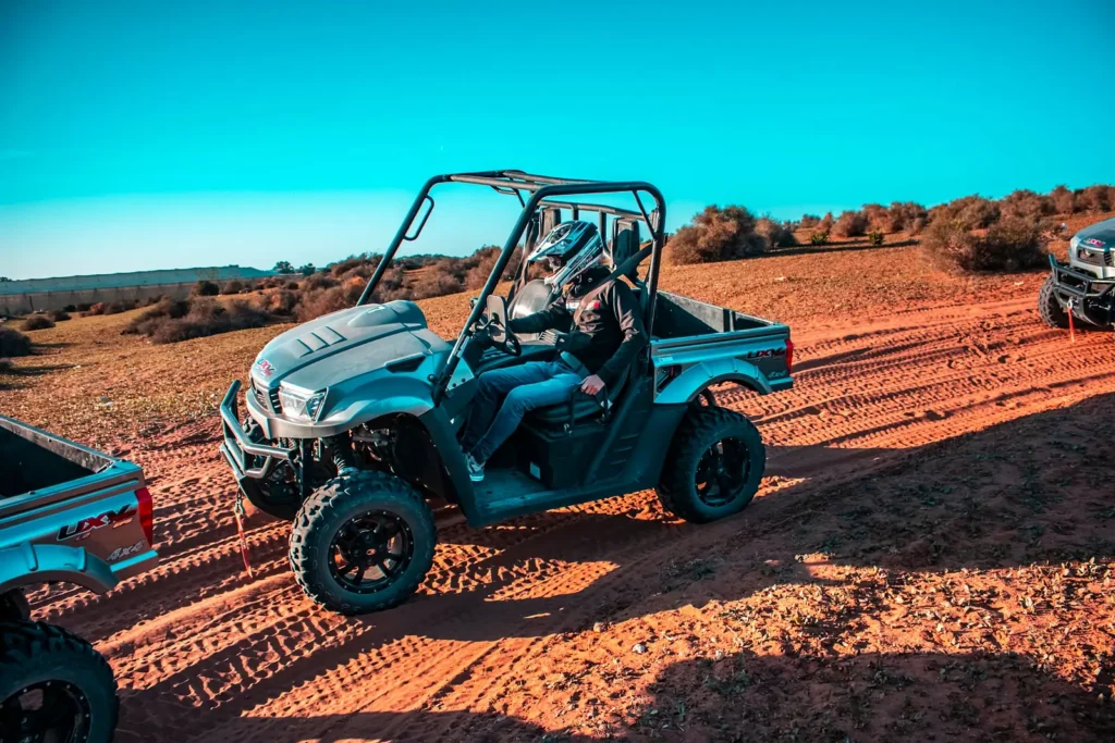 Off-road buggy with driver and passenger on red sandy tracks among desert shrubs
