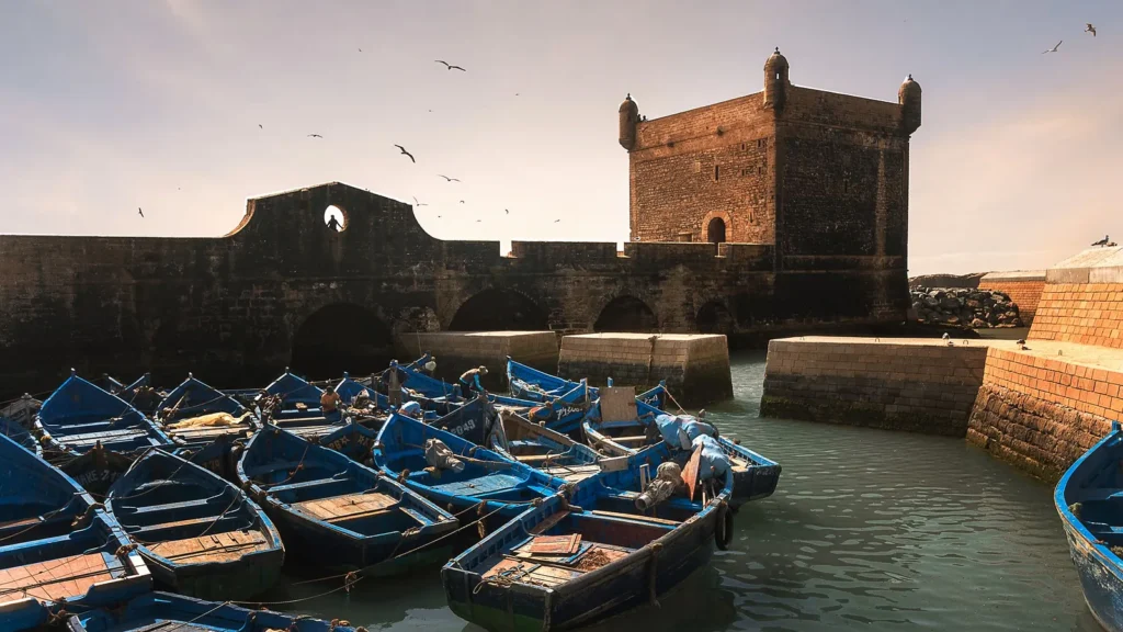 Blue fishing boats moored in Essaouira harbour beside the stone fortress