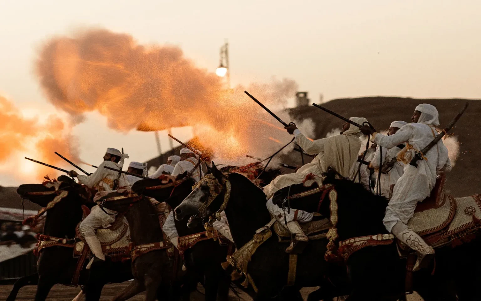 Fantasia riders in white charging on horseback as their rifles fire