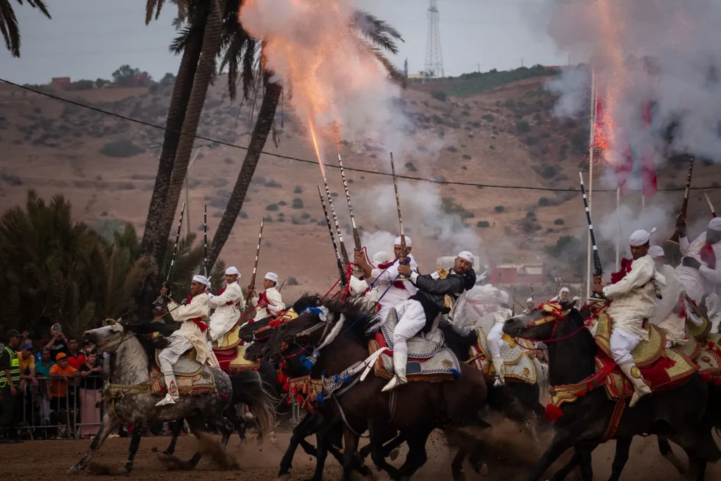 Line of horsemen in traditional dress firing powder rifles during a fantasia