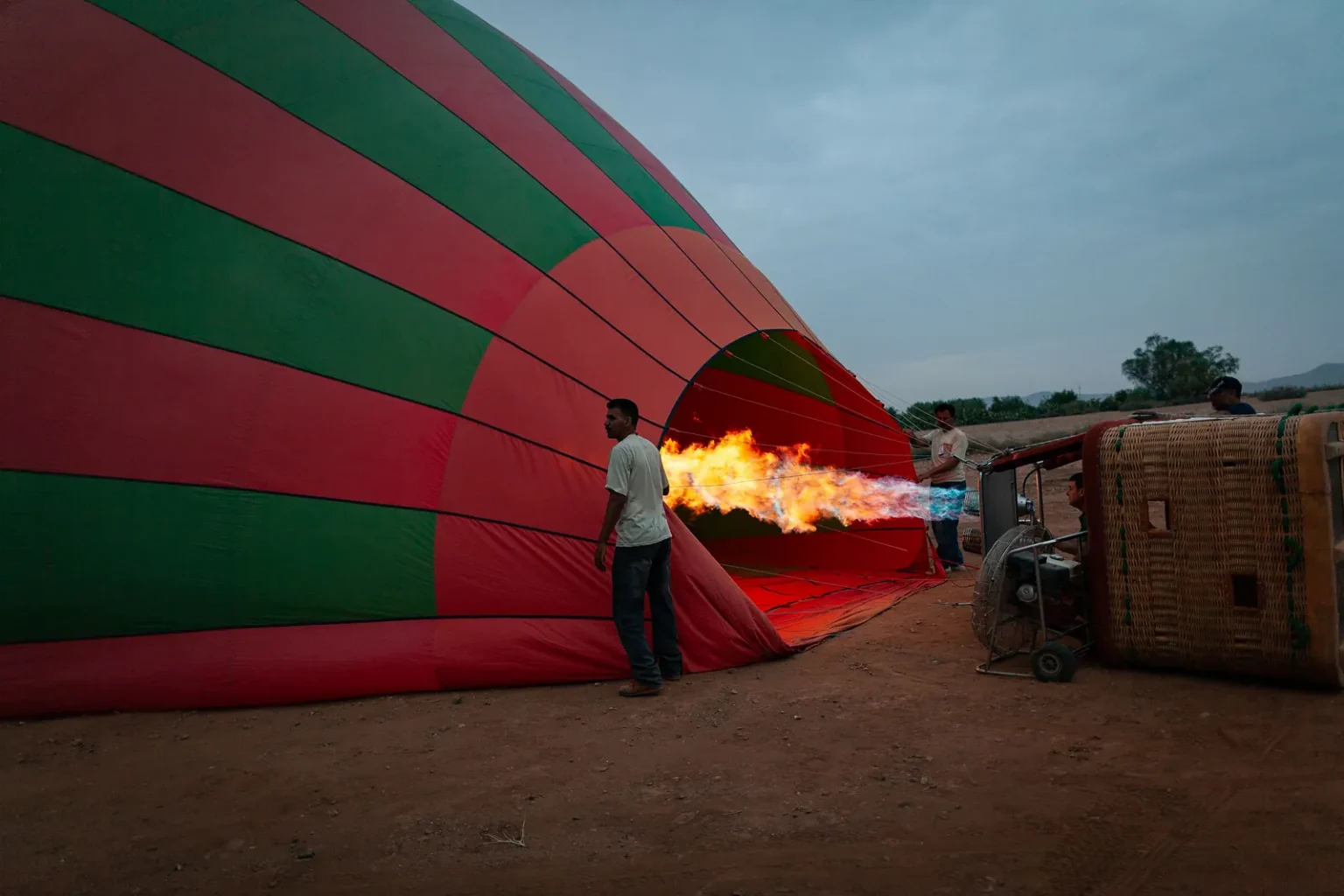 Crew inflating a red and green hot air balloon with the burner flame at dawn