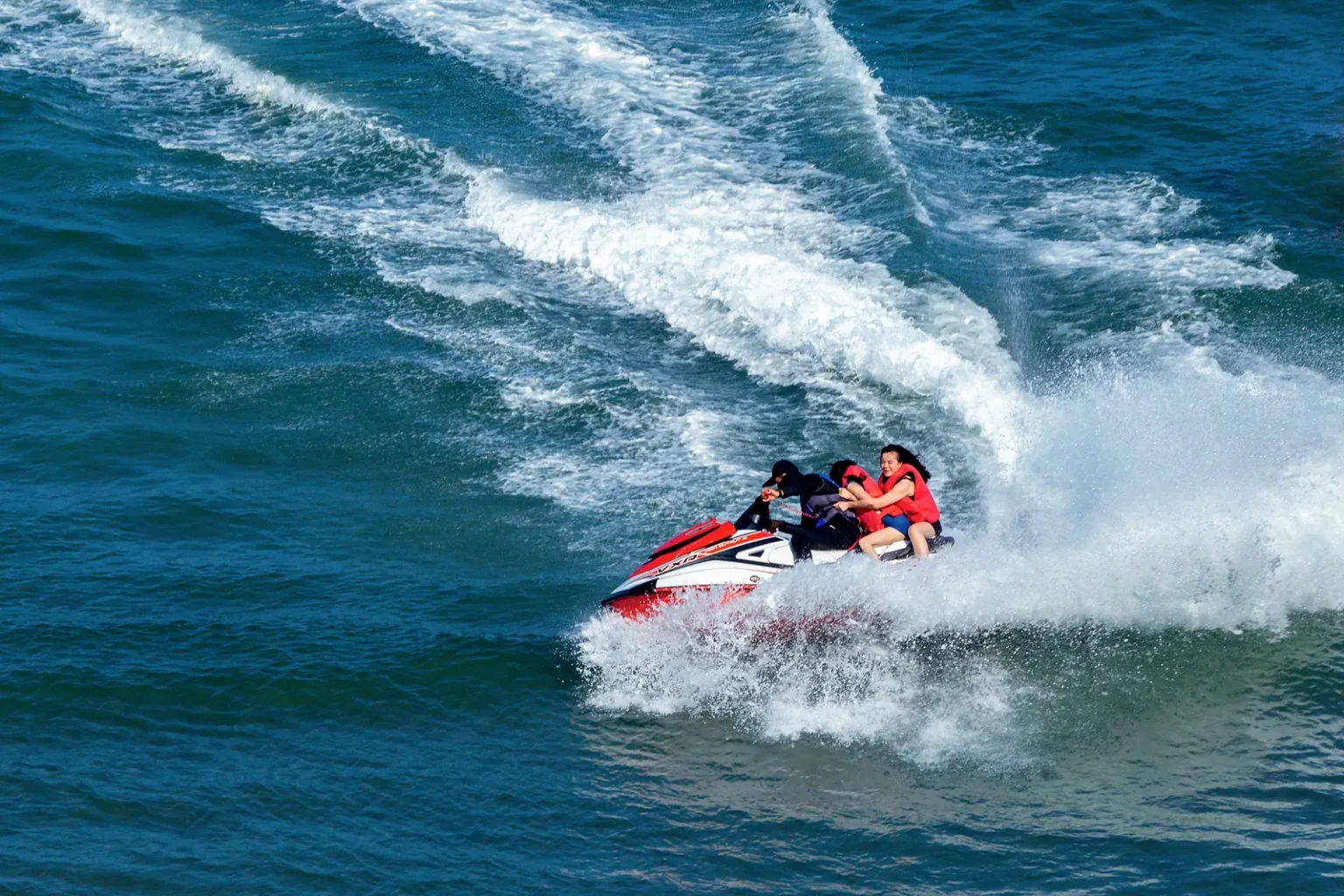Jet ski with three riders turning fast and leaving a white wake at sea