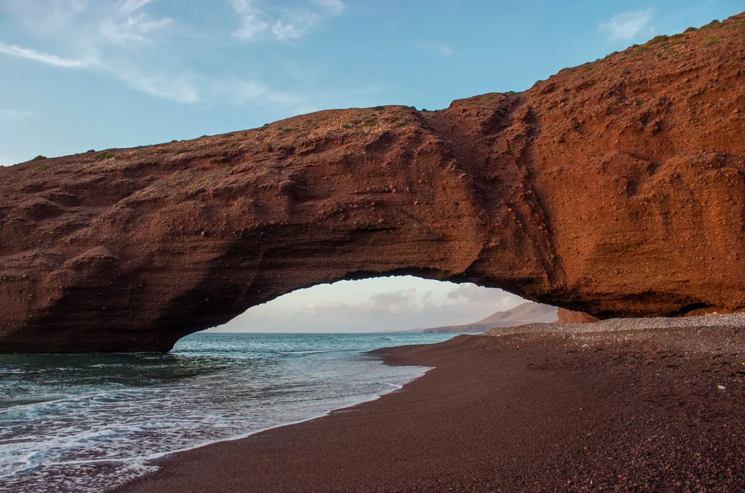 Red rock arch of Legzira beach with waves rolling onto the sand