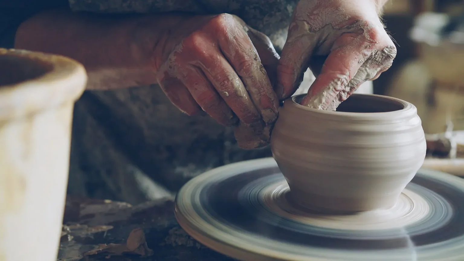 Potter's hands shaping a clay pot on a spinning wheel