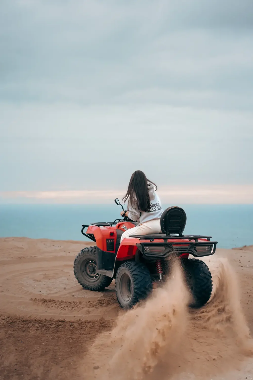 Quad bike throwing up sand on a dune edge above the ocean