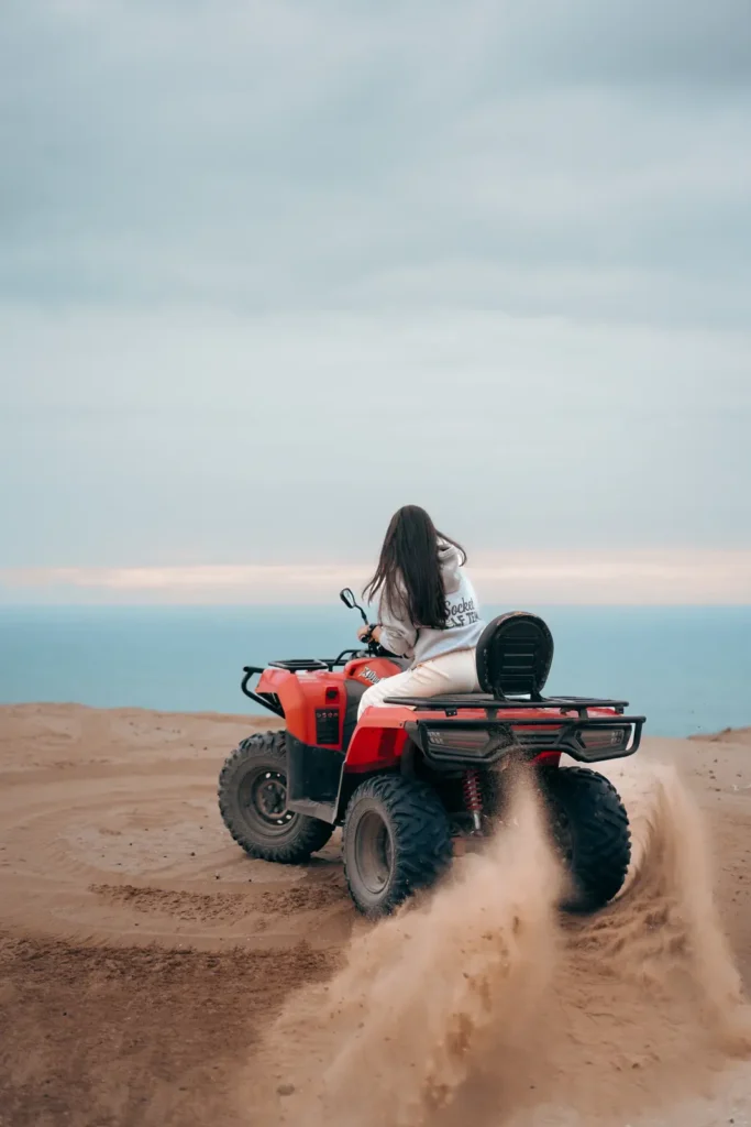 Quad bike throwing up sand on a dune edge above the ocean