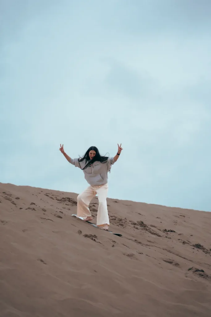 Sandboarder with arms raised on a dune in Timlalin
