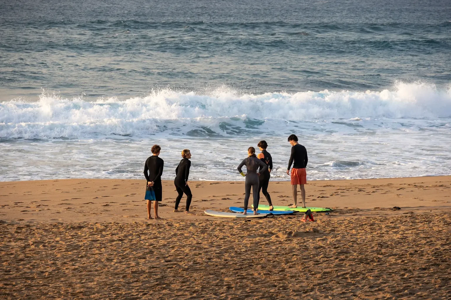 Group of beginner surfers in wetsuits with boards on the sand before a lesson